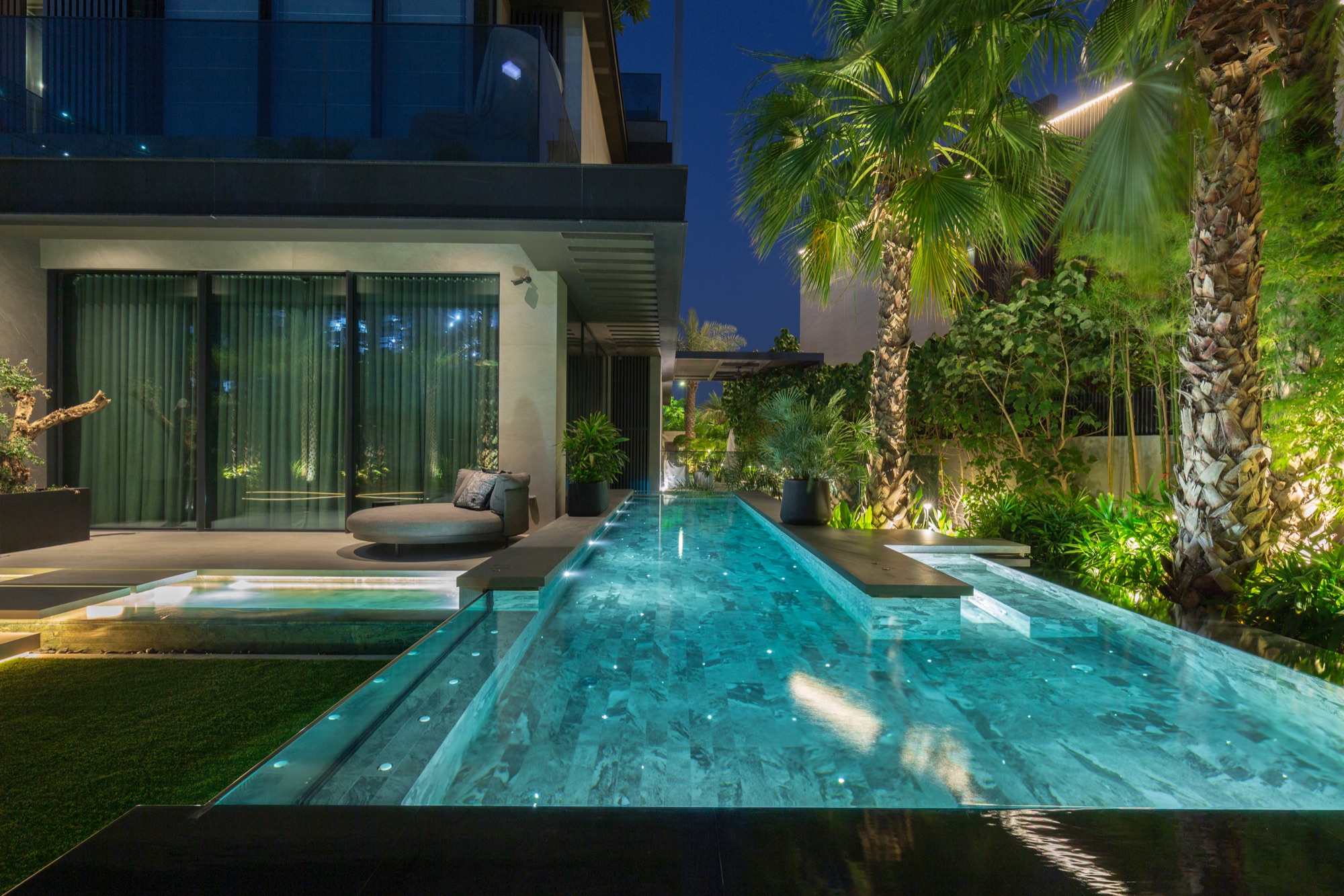 Glass-wall swimming pool surrounded by lush landscaping